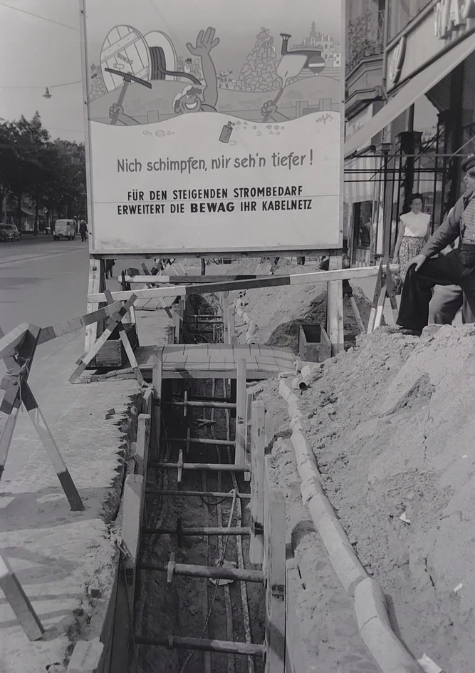 Kabelgraben mit Schild. Auf dem Schild steht: Nicht schimpfen, wir seh'n tiefer! Für den steigenden Strombedarf erweitert die BEWAG ihr Kabelnetz.