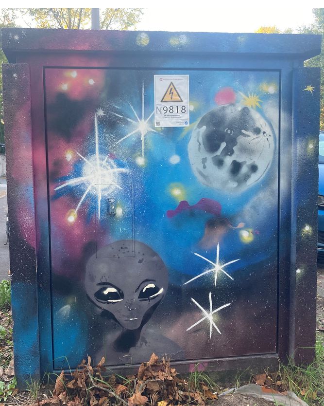 Mit einem Wandbild zum Thema Weltraum bemalter Stromkasten, auf dem die Erde mit einem Alien vor einem Sternenhintergrund dargestellt ist.