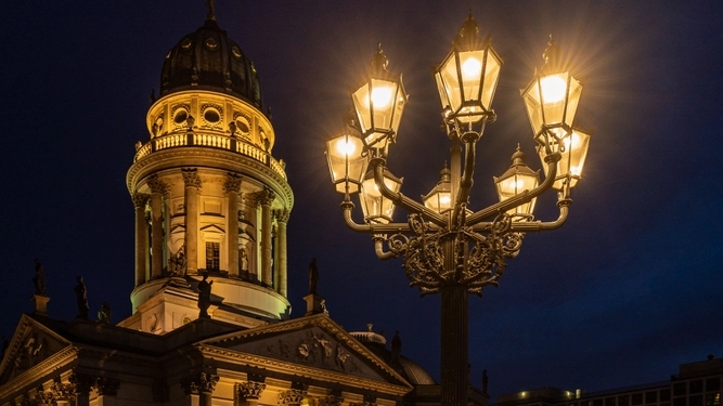 Ein leuchtender Kandelaber aus mehreren Leuchten bei Nacht vor dem Deutschen Dom am Gendarmenmarkt..