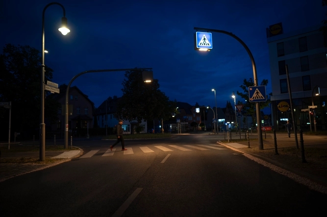 Ein Mann geht bei Nacht über eine beleuchtete Straße.