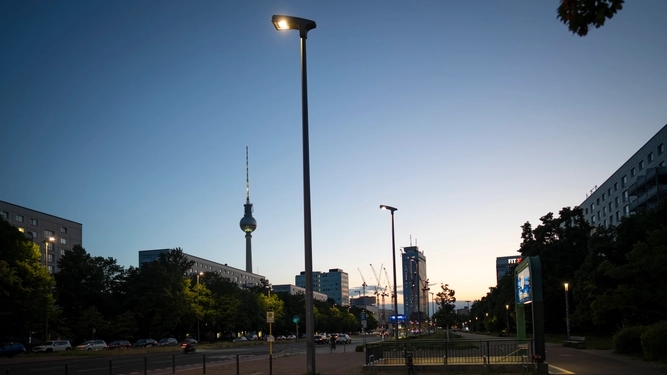Berliner Straße mit eingeschalteter Beleuchtung und dem Fernsehturm und Kränen im Hintergrund.