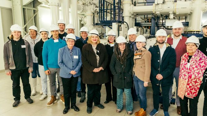 A group of people wearing hard hats stand together in an industrial setting, posing for a group photo.