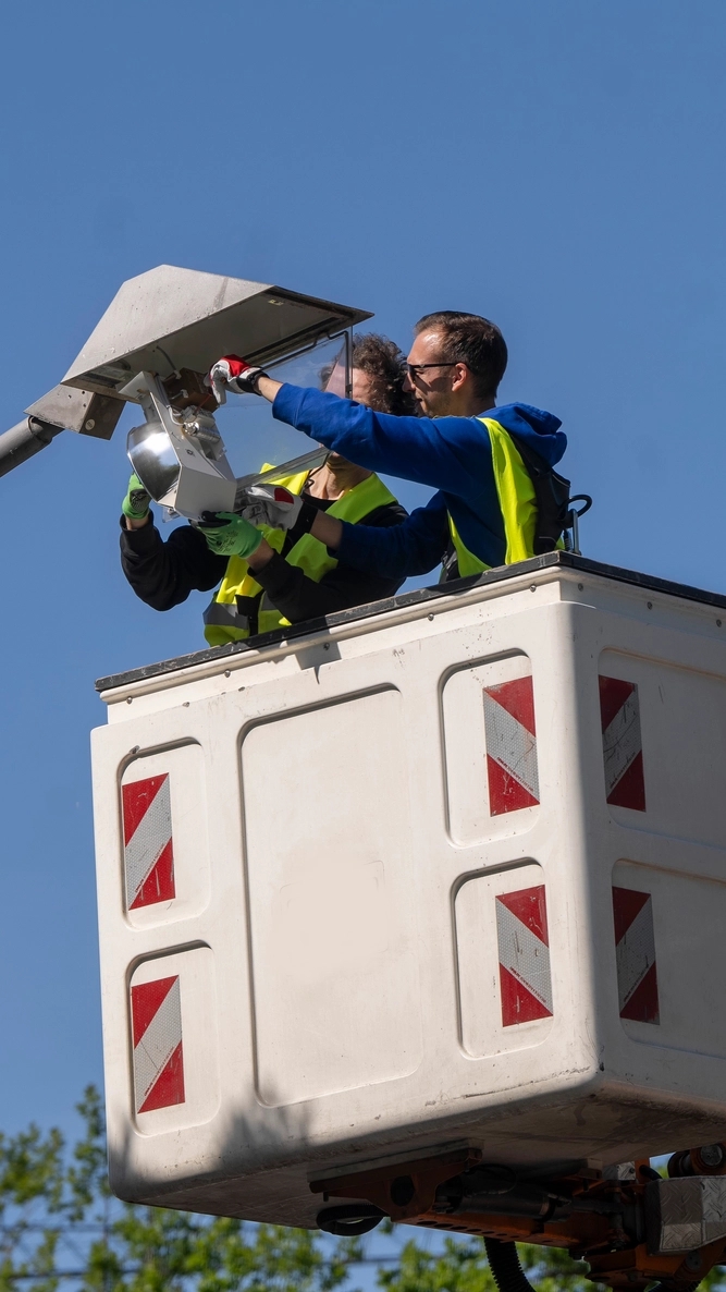 Zwei Personen in einem Hubkorb bei der Arbeit an einer Leuchte.