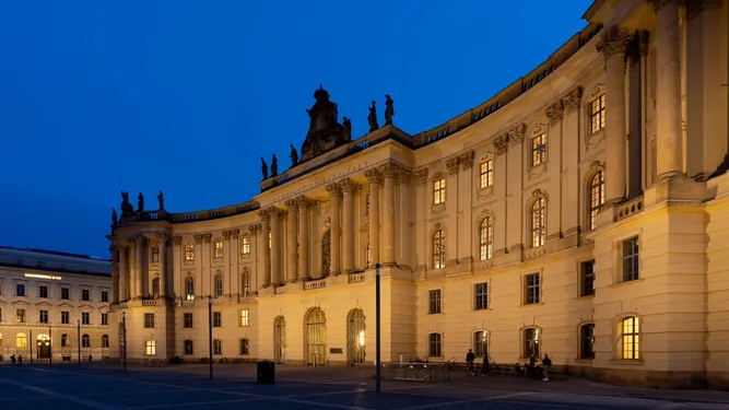 Platz mit einer angeleuchteten Fassade eines Gebäudes bei einbrechender Dunkelheit.
