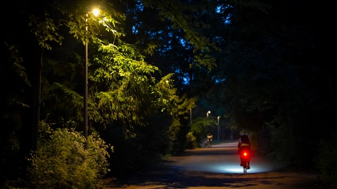 Ein Radfahrer fährt auf einem beleuchteten Parkweg bei Nacht.