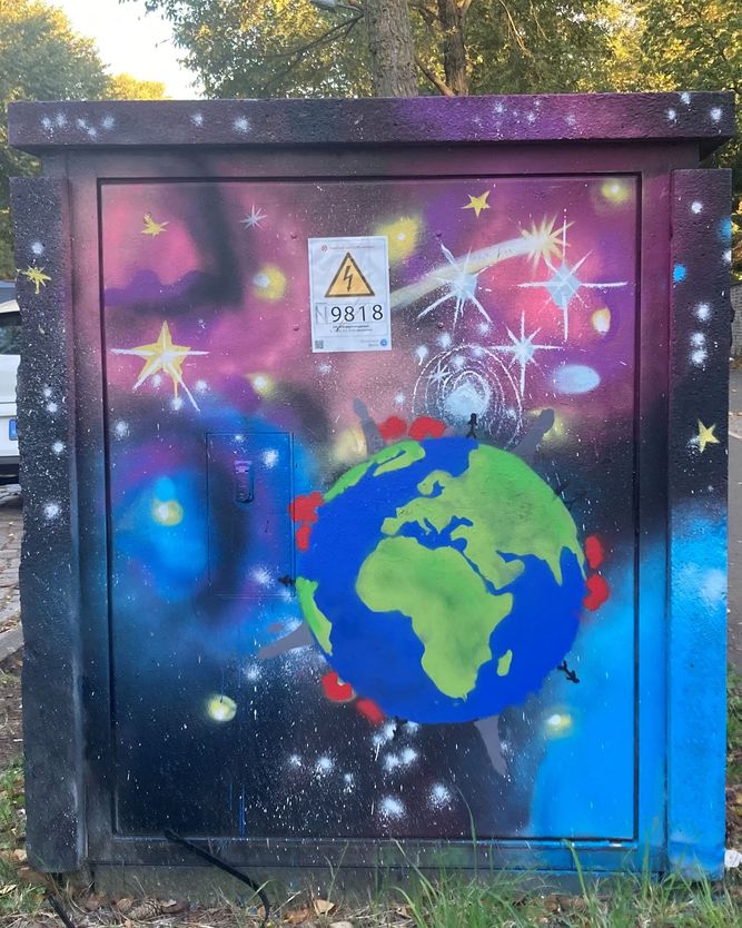 Das Kunstwerk auf einem Stromkasten zeigt eine lebendige kosmische Szene mit Sternen und Galaxien, in deren Mittelpunkt eine gemalte Erde steht.